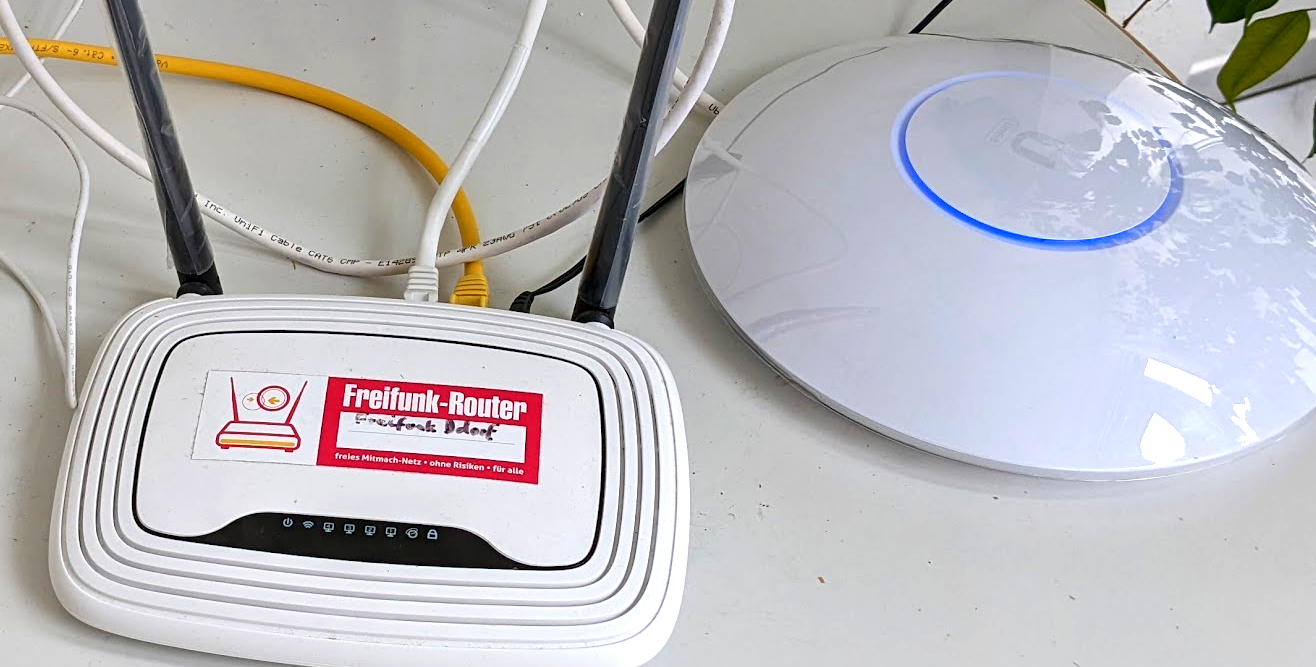 841er Plastikrouter mit Aufkleber &ldquo;Freifunk-Router&rdquo; neben einem Unifi Access-Point.